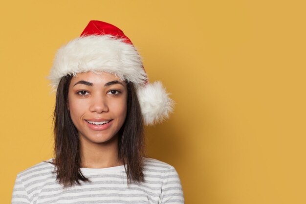 Jovem mulher negra vestindo chapéu de Papai Noel em fundo amarelo