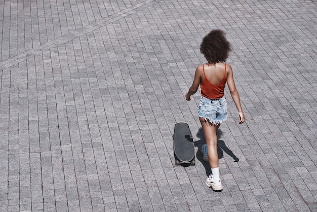 Jovem mulher no estilo livre na rua, andando perto do skate