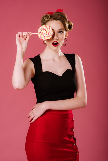 Jovem mulher no estilo retrô, posando com um doce pirulito no fundo rosa. retrato de pin-up