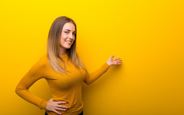 Jovem mulher no fundo amarelo apontando para trás e apresentando um produto