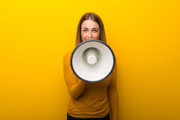 Jovem mulher no fundo amarelo que shouting através de um megafone para anunciar algo