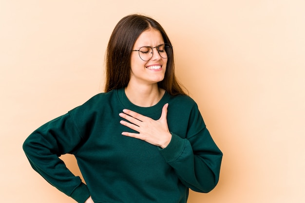 Jovem mulher no riso bege mantendo as mãos no coração, conceito da felicidade.