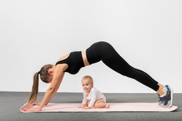 Jovem mulher no treino de sportswear junto com seu bebê. Mãe feliz com filho fazendo exercícios de ioga de prancha. Conceito de estilo de vida ativo e maternidade