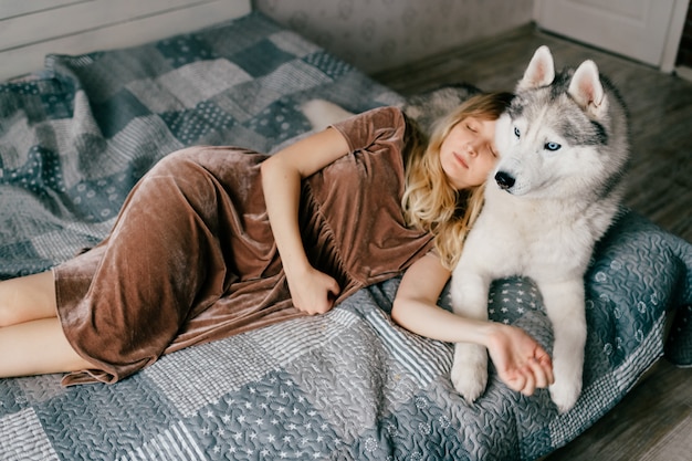 Foto jovem mulher no vestido marrom que encontra-se na cama em casa com filhote de cachorro ronco.