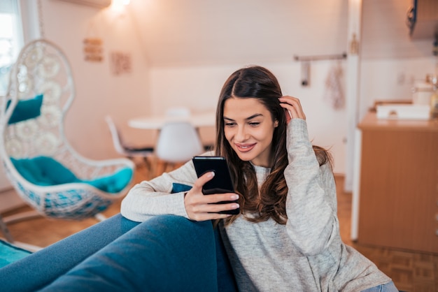 Jovem mulher ocasional que usa o telefone celular em casa.