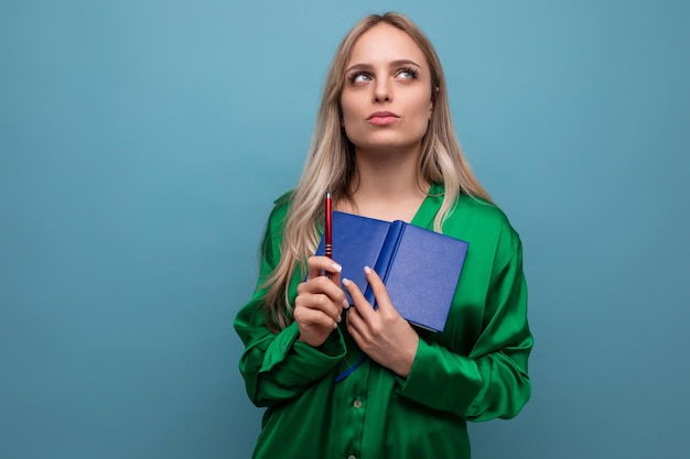 Jovem mulher olhando para o trabalho segurando o bloco de notas e lápis sobre fundo azul brilhante