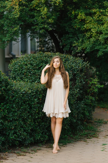 Jovem mulher ou menina em um vestido leve voa com os pés descalços através de um parque da cidade no verão