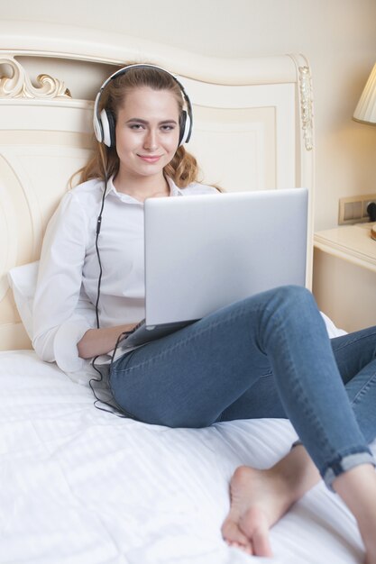 Jovem mulher ouvindo música e usando o laptop na cama