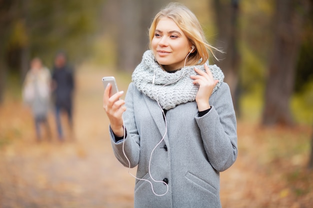 Jovem mulher ouvindo música na floresta de outono
