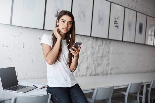 Jovem mulher ouvindo reflexões on-line em seu telefone inteligente chegando cedo ao local de trabalho