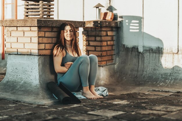 Jovem mulher pensando em algo enquanto se prepara para um treinamento de ioga em um terraço.