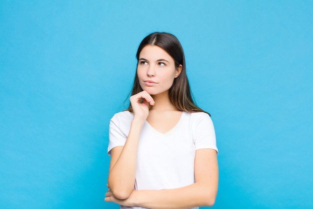 Jovem, mulher, pensativo, pensando ou imaginando idéias, sonhando acordado e olhando para copiar o espaço na parede azul