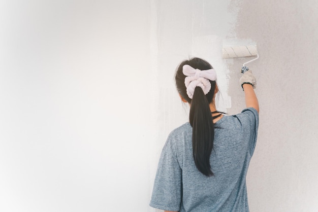 Jovem mulher pintando as paredes com um rolo usando tinta branca.