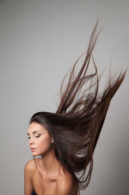 Jovem mulher posando com seu cabelo comprido jogado para cima. foto de estúdio vertical.