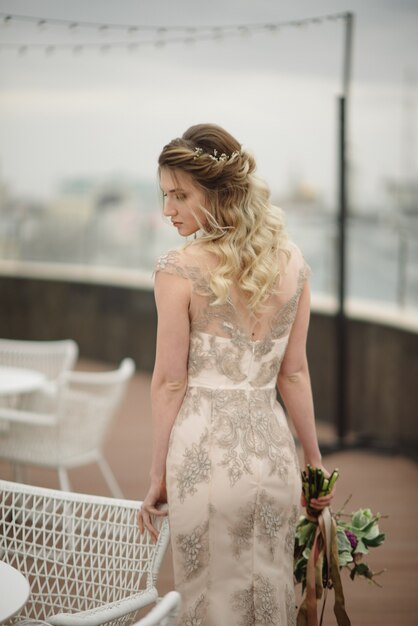 Jovem mulher posando em um vestido longo de renda leve com um buquê de flores nas mãos dela