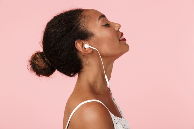 Jovem mulher posando isolada sobre uma parede rosa ouvindo música com fones de ouvido