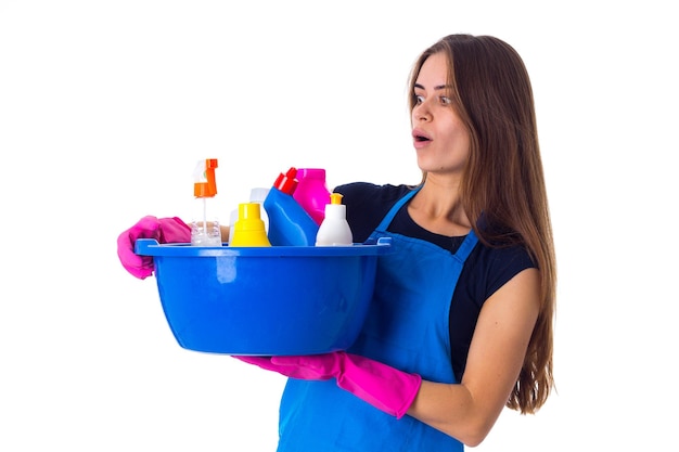 Jovem mulher positiva com luvas vermelhas segurando coisas de limpeza na bacia azul