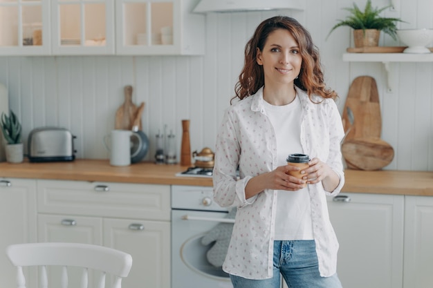 Jovem mulher positiva com telefone em sua cozinha contemporânea elegante Interior escandinavo branco