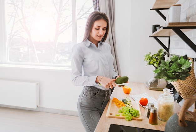 jovem mulher preparando comida de legumes em pé na cozinha