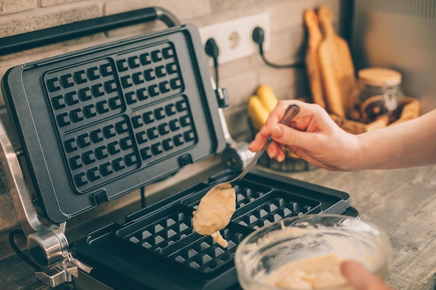 Foto jovem mulher preparando waffles belgas na cozinha processo de cozimento