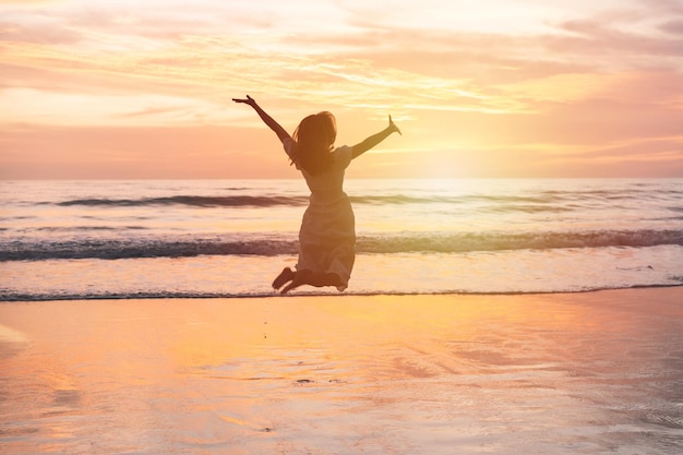 Jovem mulher pulando na praia ao pôr do sol lindo conceito de férias de verão