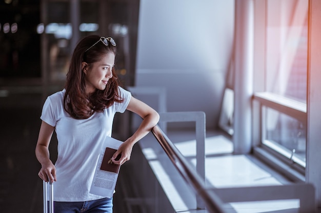 Jovem mulher puxando mala no moderno terminal do aeroporto Viajando com sua bagagem enquanto espera pelo transporte Vista traseira Copie o espaço