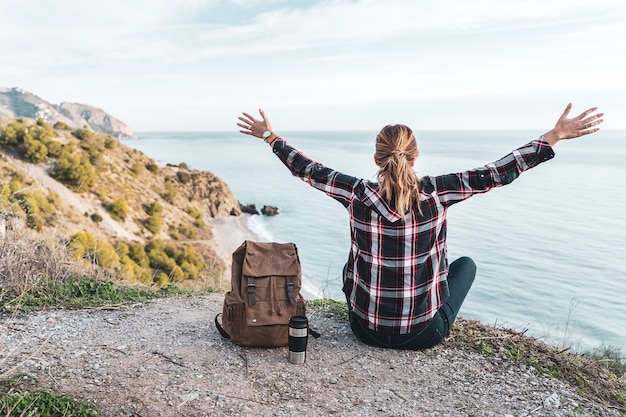 Foto jovem mulher quadril com braços abertos e uma mochila explora a costa em um lindo dia. conceito de exploração e aventuras