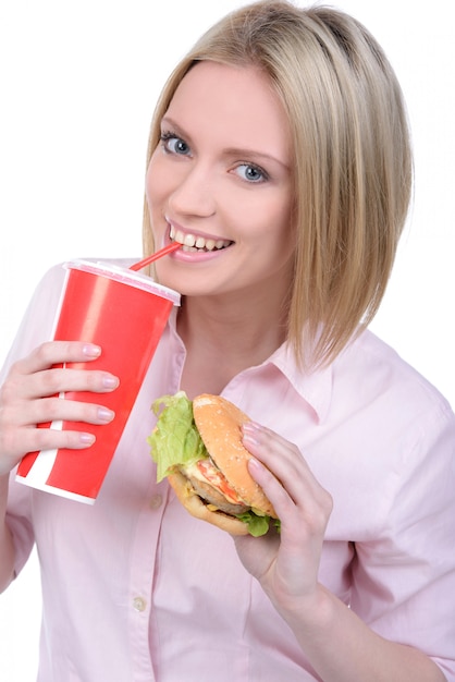 Jovem mulher que come o fast food e que bebe a soda.