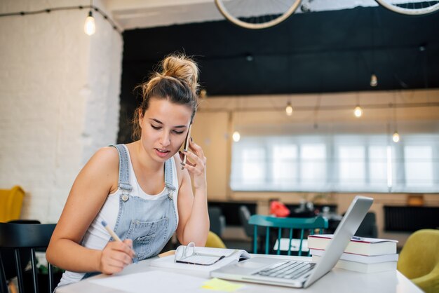 Jovem mulher que faz anotações ao falar em um telefone no lugar público.