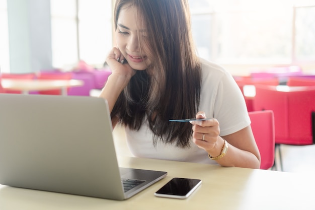 Jovem mulher que guarda o cartão de crédito disponível e que usa o portátil do computador para comprar em linha.