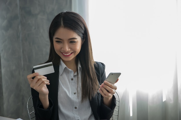 Jovem mulher que guarda o cartão de crédito que compra em linha do laptop.