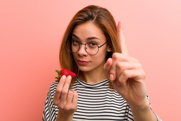 Jovem mulher que guarda uma morango que mostra o número um com dedo.