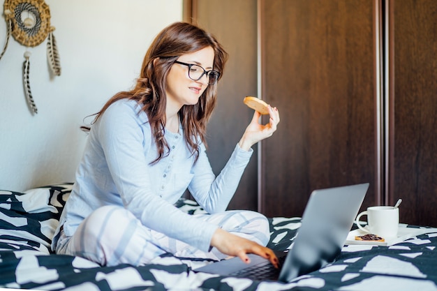Foto jovem mulher que trabalha na cama em casa com computador.