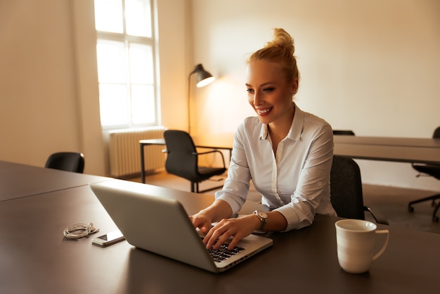 Jovem mulher que trabalha na mesa de escritório moderna com um laptop