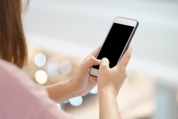 Jovem mulher que usa o telefone esperto com mãos no fundo do bokeh.