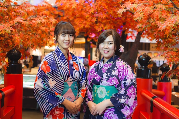 Jovem mulher que veste o quimono tradicional japonês na cor do outono com a ponte de madeira vermelha. Japão