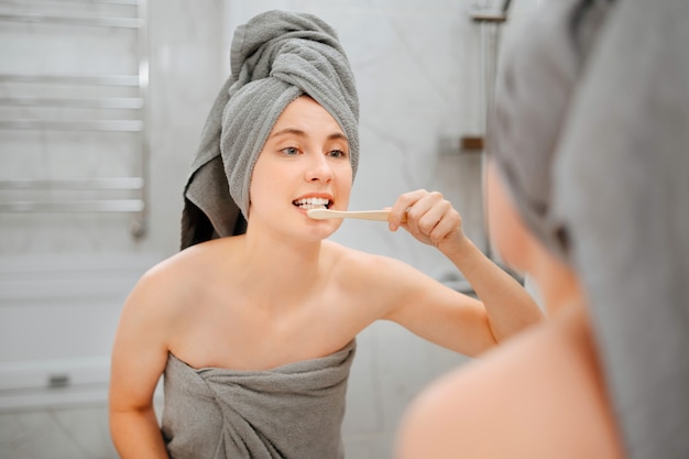 Jovem mulher realiza cuidados matinais no banheiro, escovando os dentes da cárie. Conceito de saúde e odontologia.
