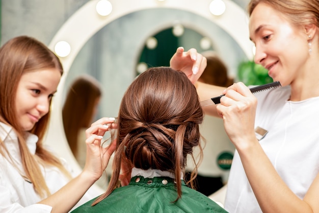 Jovem mulher recebendo maquiagem e penteado por maquiador profissional e cabeleireiro no salão de beleza.