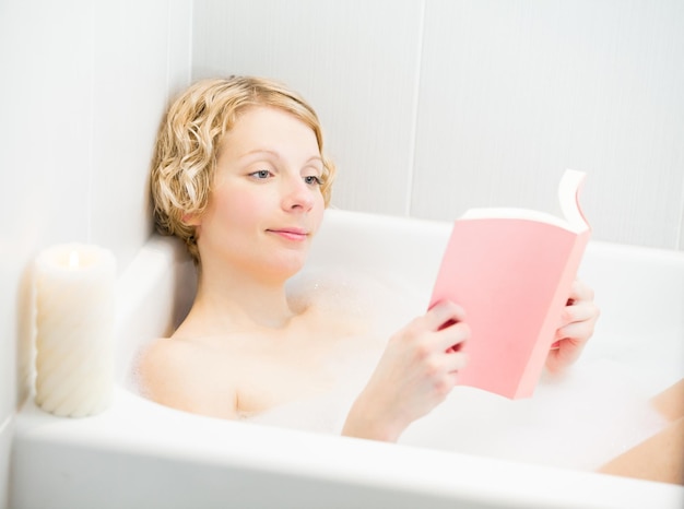 Jovem mulher relaxando e lendo um livro no banho