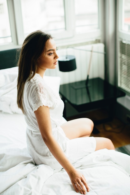 Jovem mulher relaxando em uma cama branca pela manhã