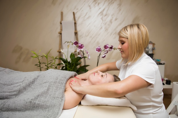 Jovem mulher relaxante durante a massagem do corpo no ombro no spa