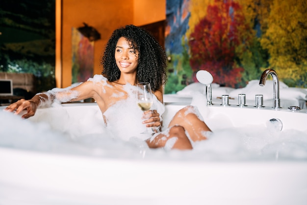 Jovem mulher relaxante no banho de hidromassagem coberto de espuma