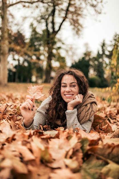 Jovem mulher relaxante parque outono, olhando para a câmera.