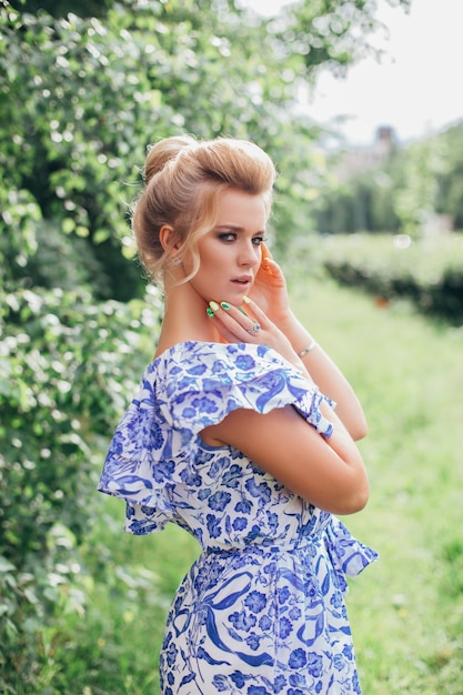 Jovem mulher romântica com vestido de flor azul com maquiagem e penteado no jardim verde de verão