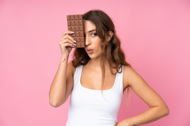 Jovem mulher rosa tomando uma tablete de chocolate e surpreendeu