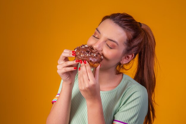 Jovem mulher ruiva comendo rosquinhas de chocolate deliciosas. jovem comendo rosquinhas saborosas