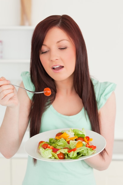 Jovem, mulher ruiva, desfrutando de uma salada mista na cozinha