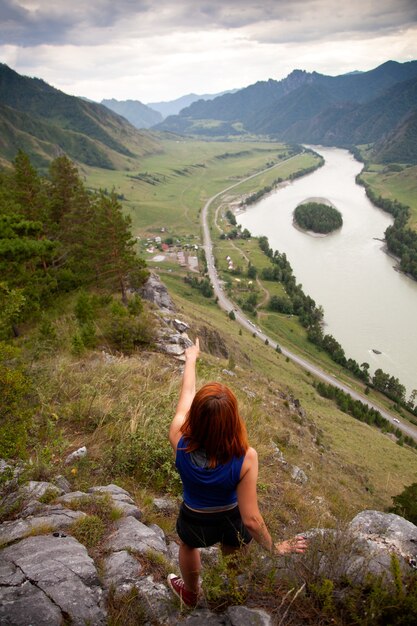 Jovem mulher ruiva sentada na montanha pela manhã e aponta o dedo para a montanha e o sol. O conceito de uma mulher livre. Solidão e pacificação nas montanhas