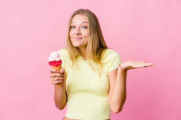 Jovem mulher russa comendo um sorvete isolado duvidando e encolhendo os ombros em um gesto de questionamento.