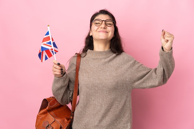 Jovem mulher russa segurando uma bandeira do Reino Unido isolada na parede rosa fazendo um gesto forte